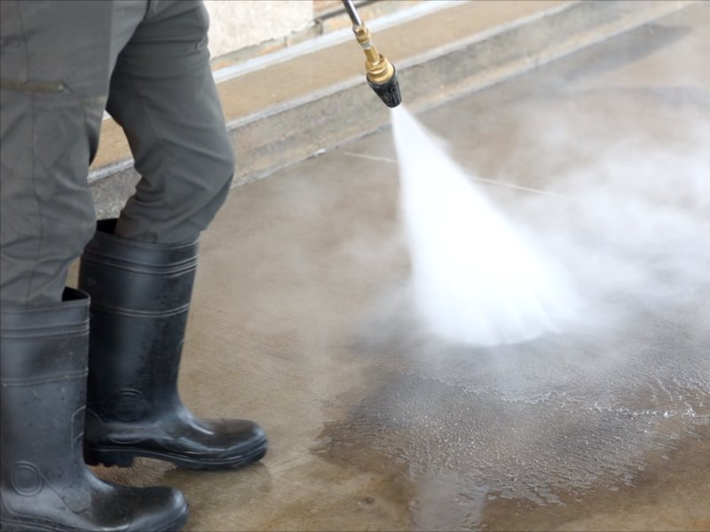 pressure washing professional in black boots cleaning concrete